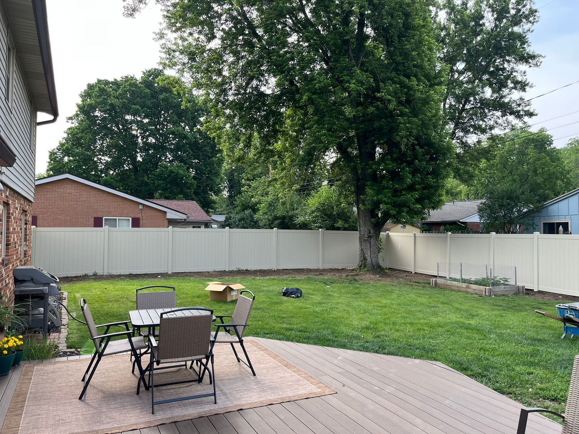 Backyard with beige fence, deck, table, chairs, and large tree.