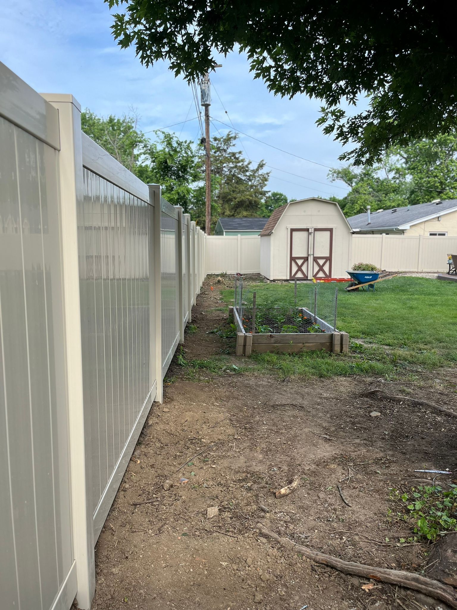 Beige vinyl fence along a dirt path, leading to a garden and shed in a backyard.