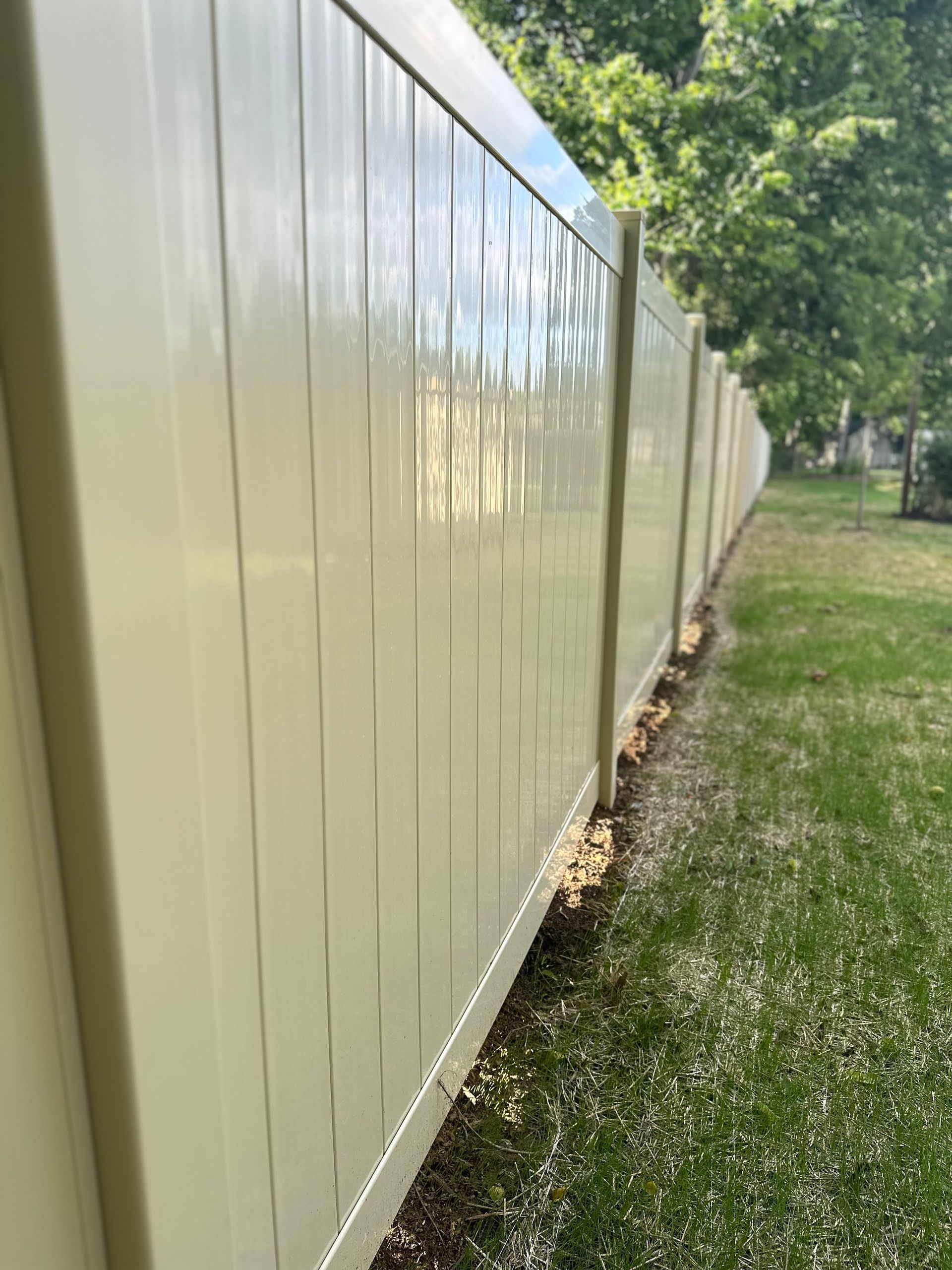Tan vinyl fence in a grassy yard, partially obscured by bright sunlight.