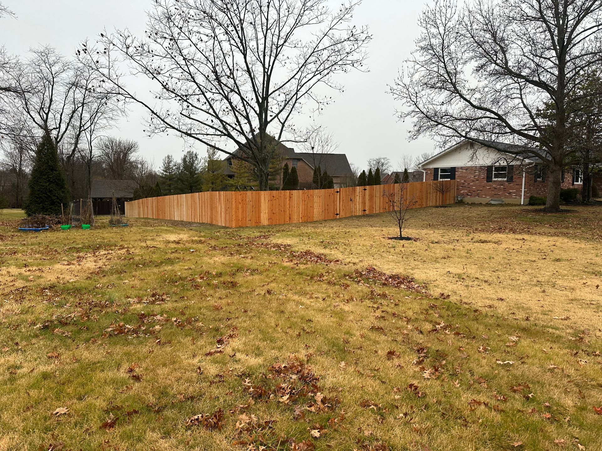 A wooden fence surrounds a grassy yard on an overcast day.