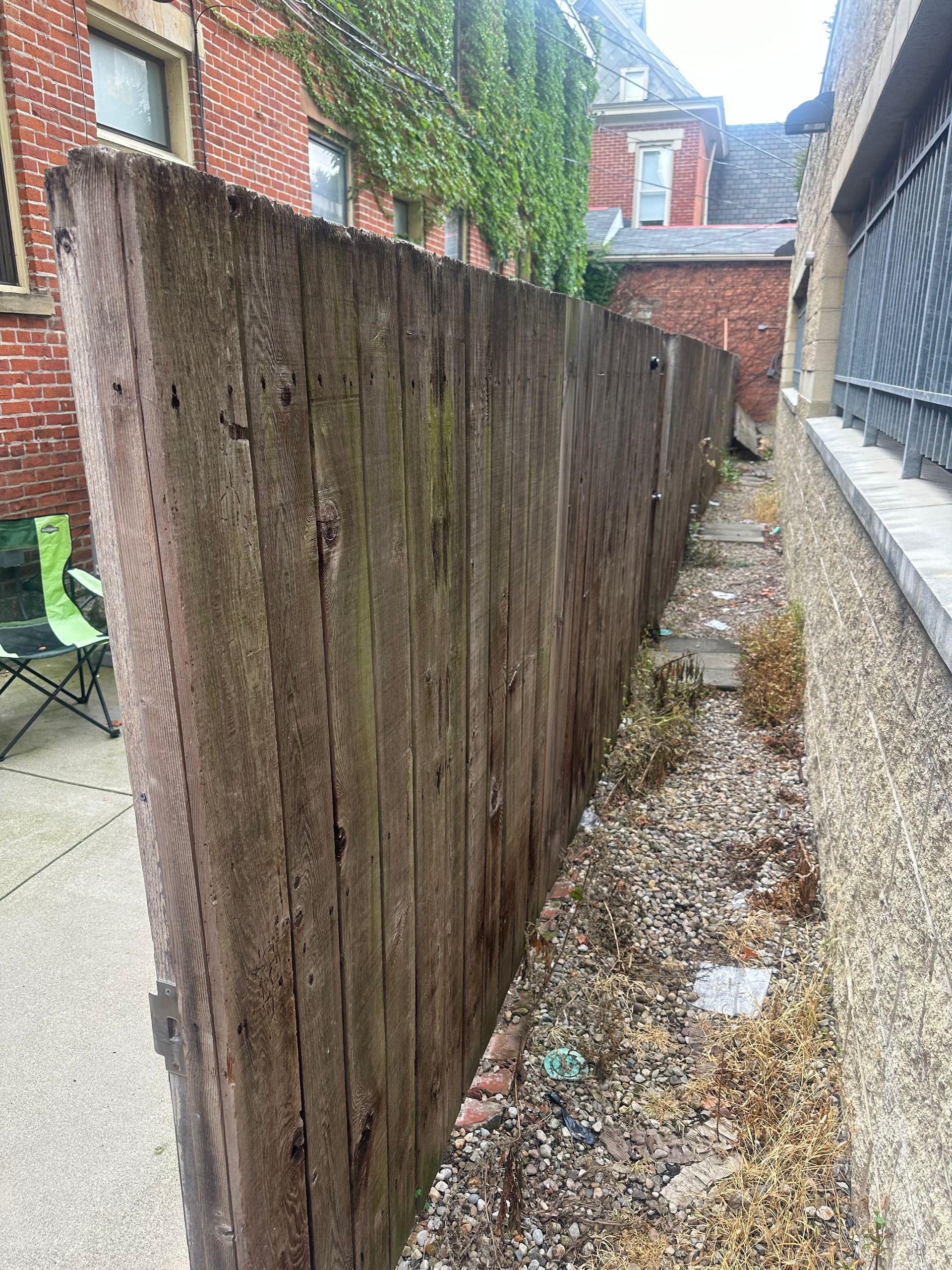 Wooden fence next to a narrow gravel-filled area between brick buildings.