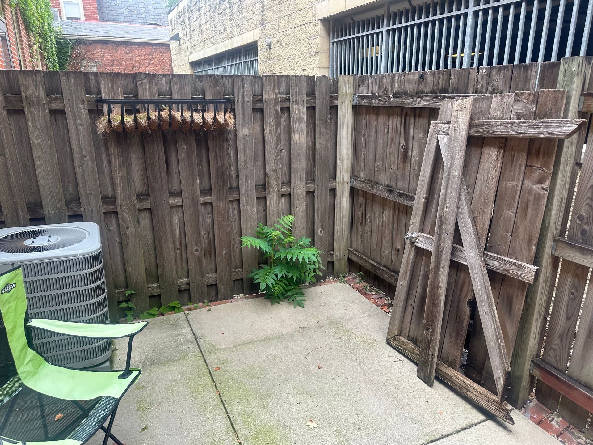 Backyard patio with wooden fence, air conditioner, green chair, and leaning wooden frame.