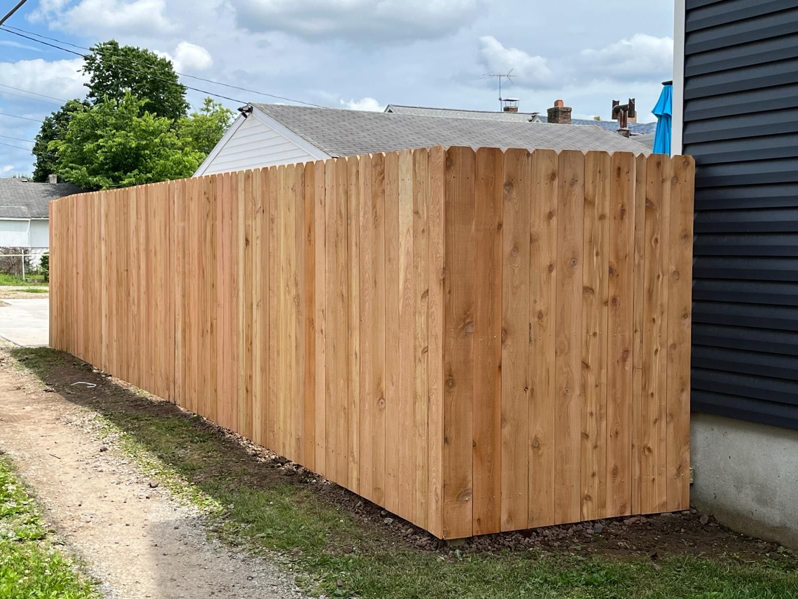 Wooden privacy fence along a side yard with a gravel path, green grass, and houses in the background.