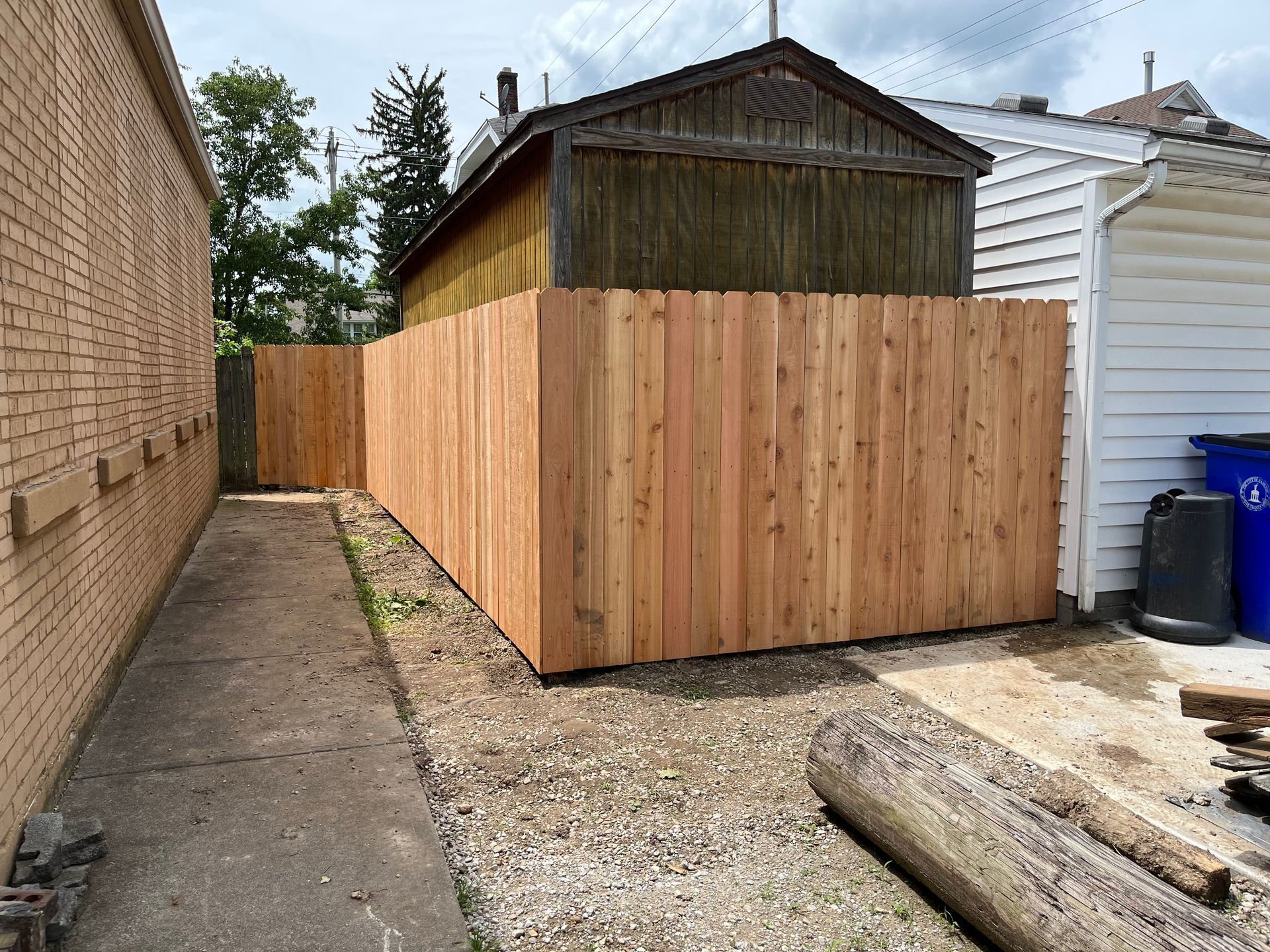New wooden fence in an alleyway, beside a brick building and a white house.