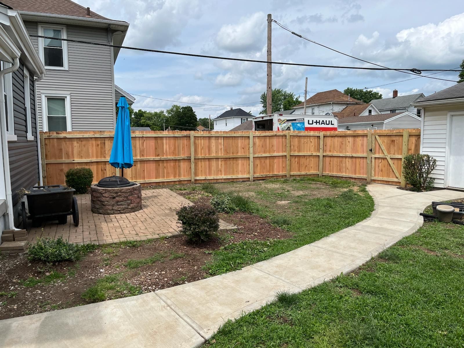 Backyard with a wooden fence, fire pit, patio, and a concrete path.