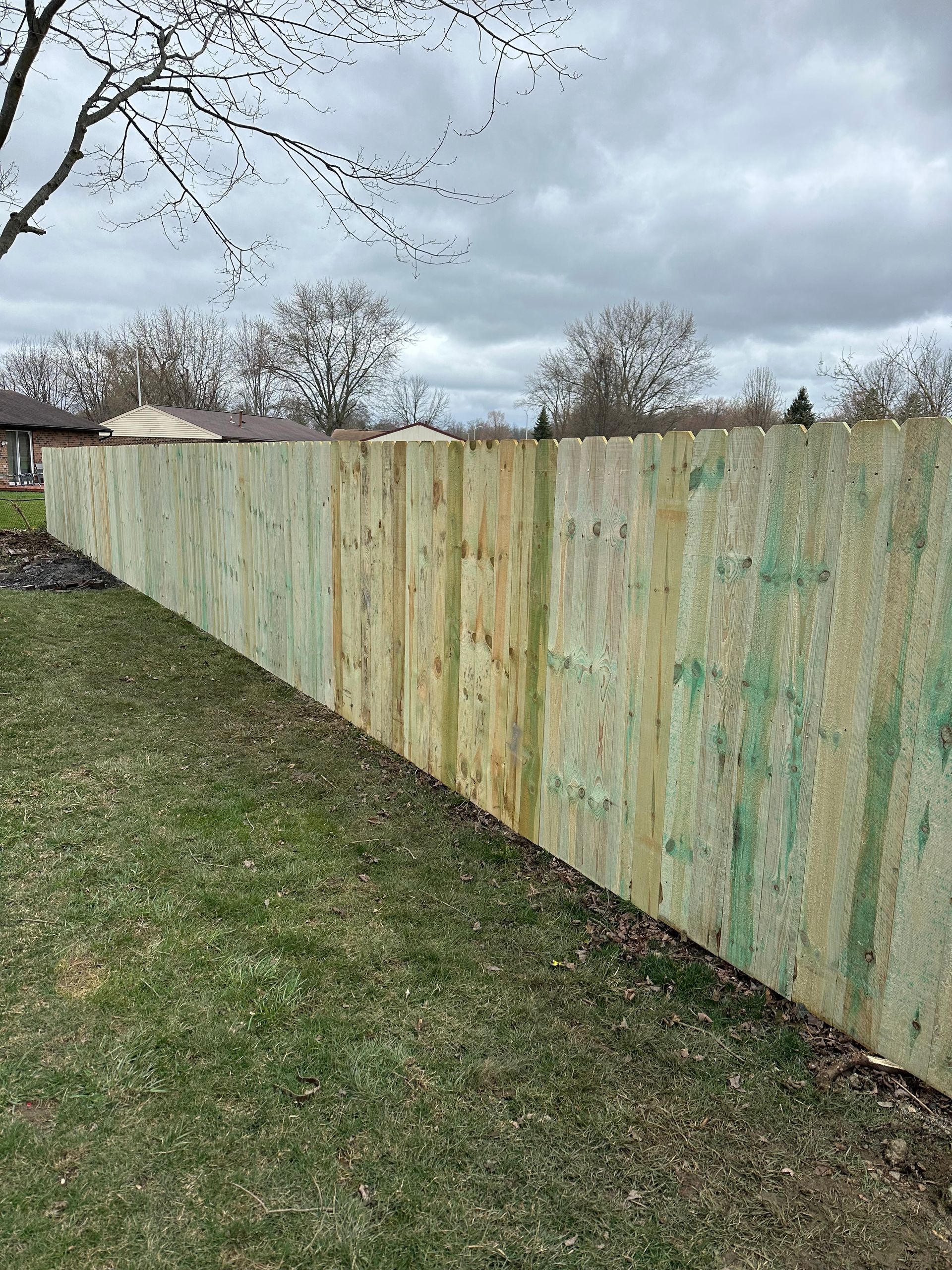 Wooden privacy fence along grassy yard under cloudy sky.