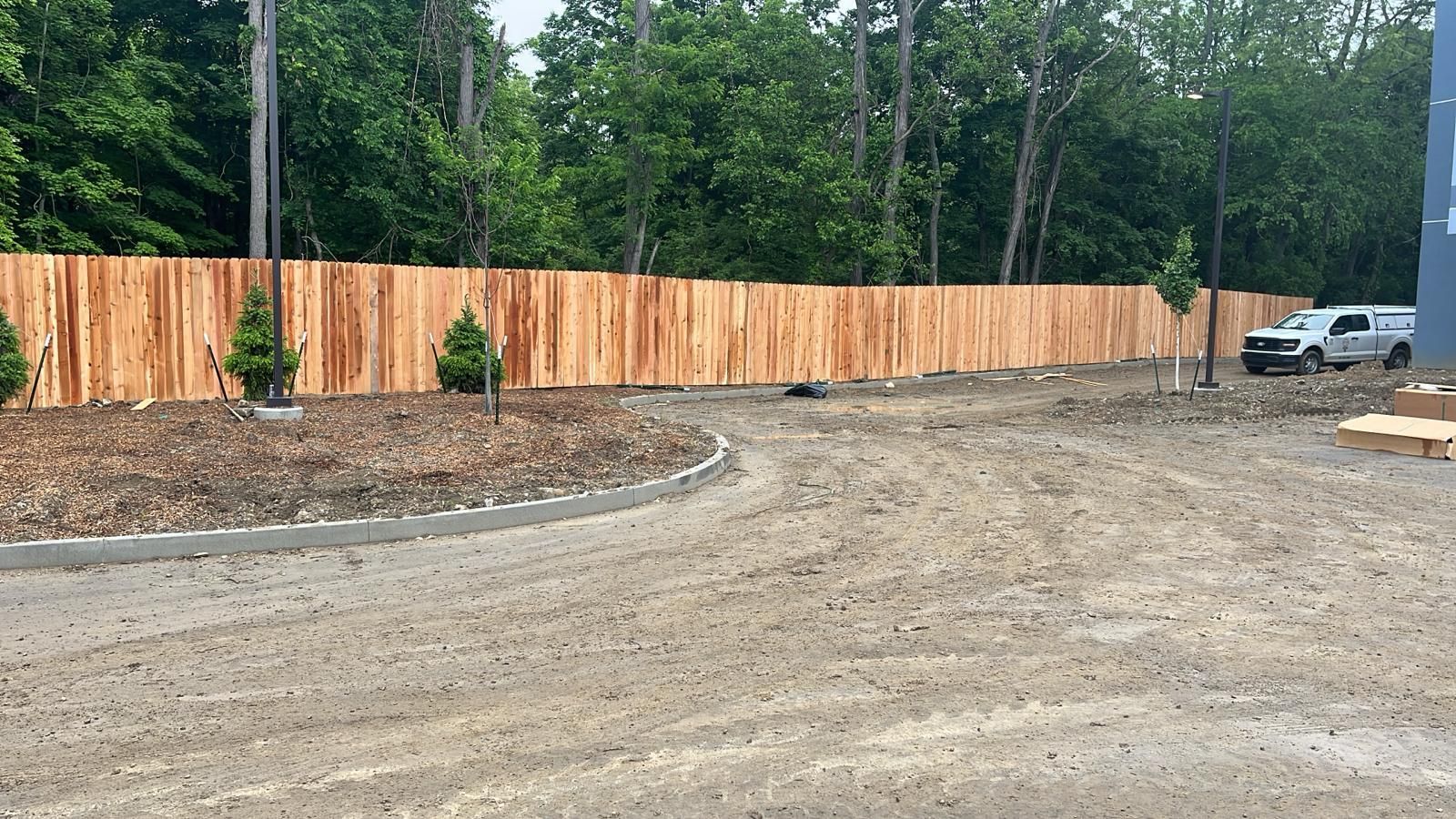 Gravel driveway with a wood fence and trees in the background. A truck is parked to the right.