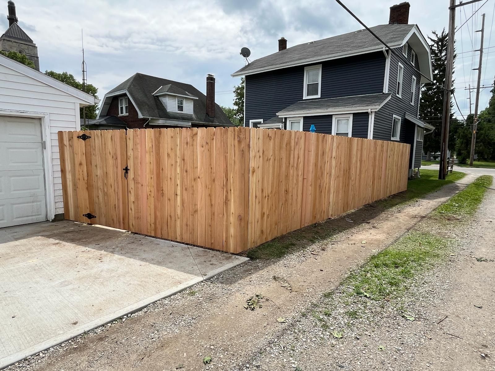 Wooden fence surrounding a yard next to a two-story blue house and a white garage.