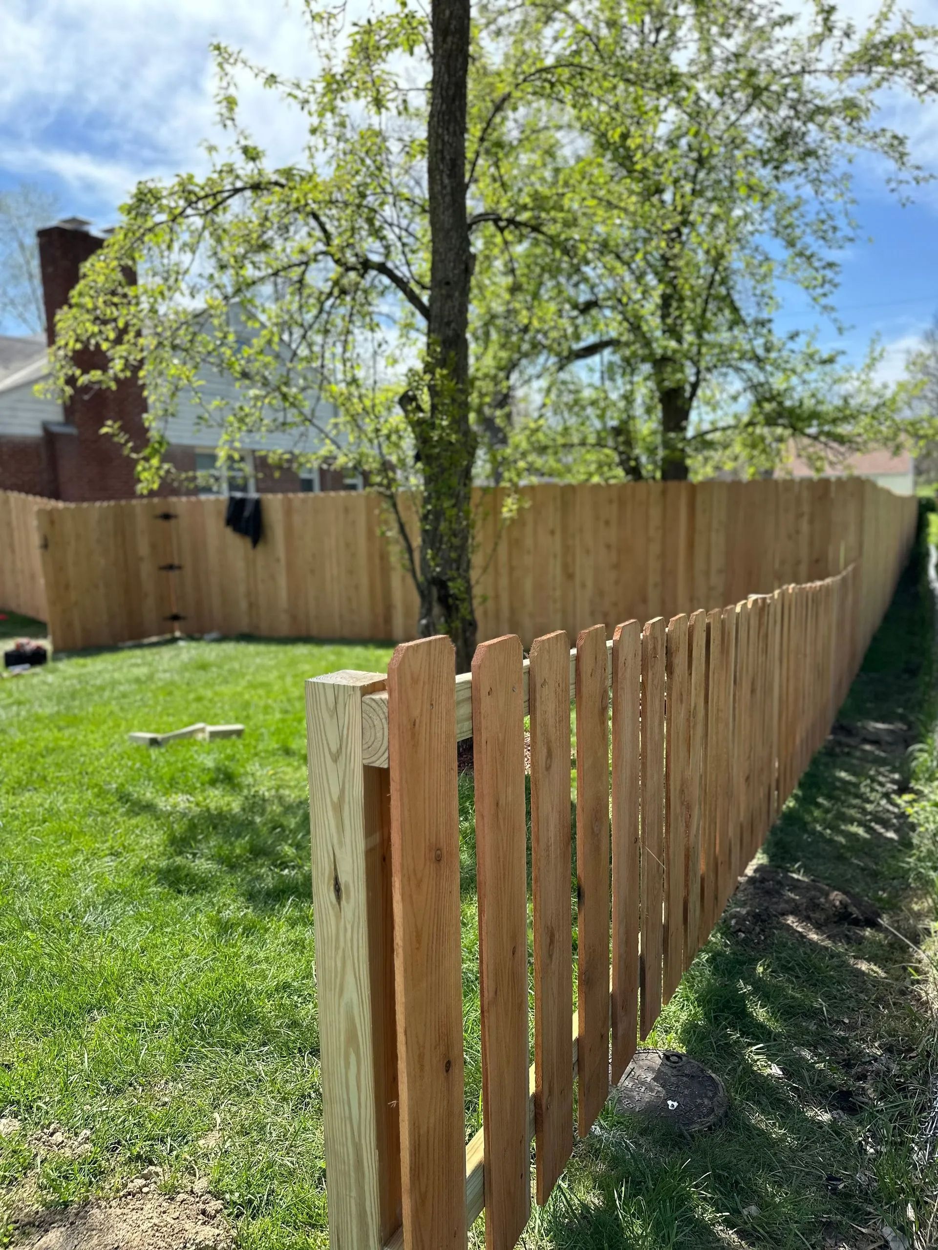 Wooden fence in a yard, trees and house in the background. Bright day.