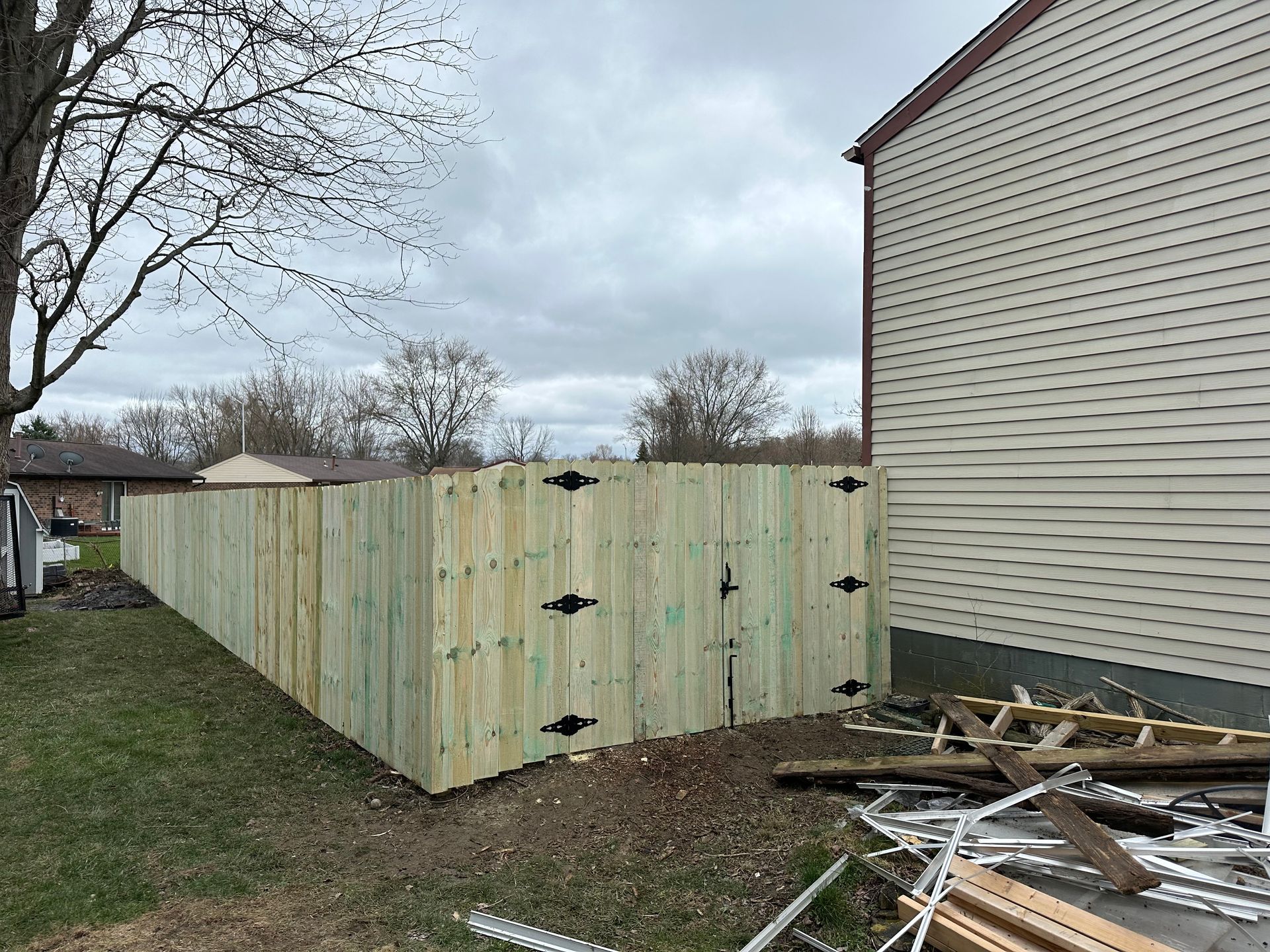 Wooden fence in backyard next to a house under a cloudy sky.