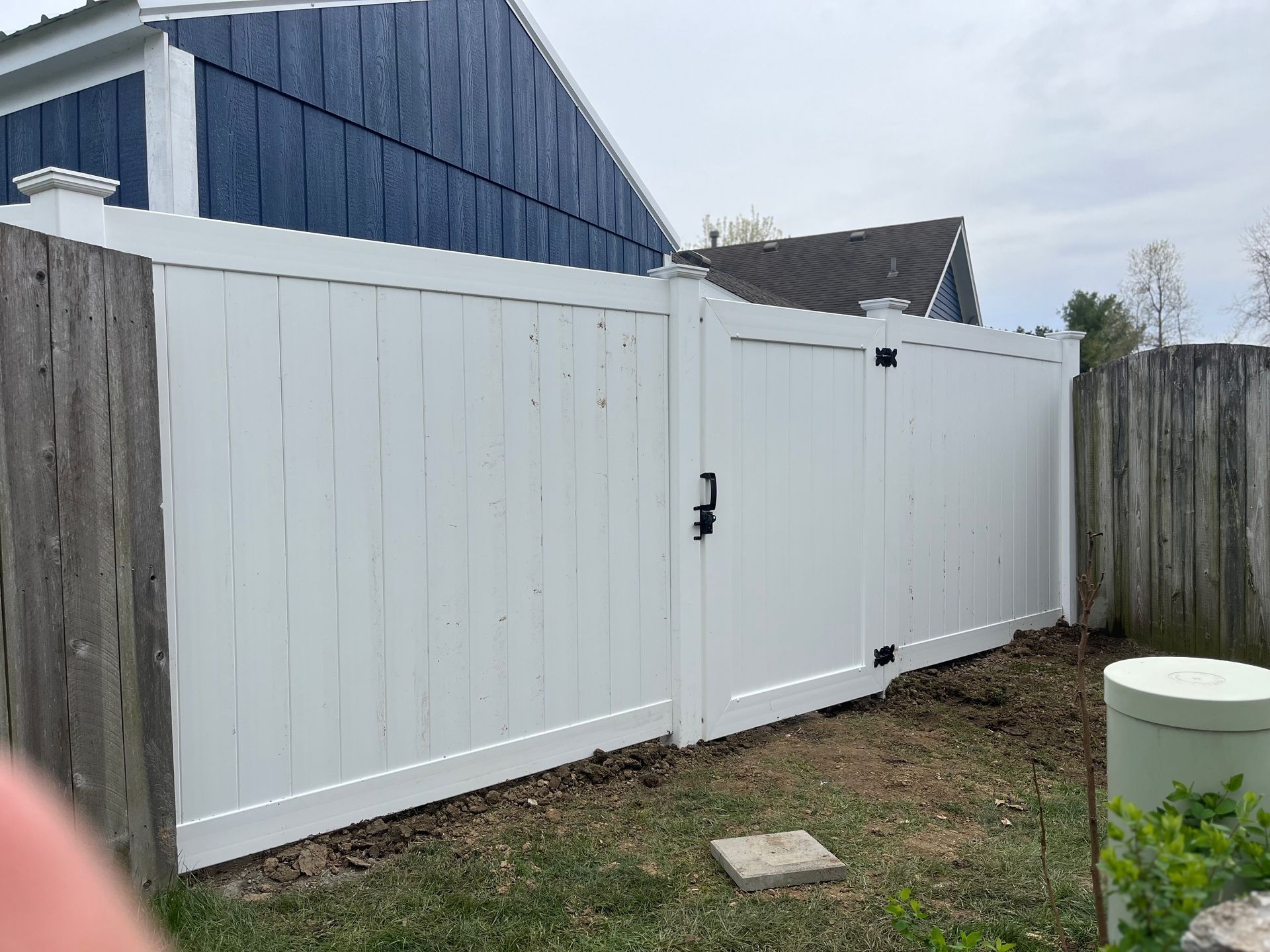White vinyl fence with gate, set against a blue house and a wooden fence.