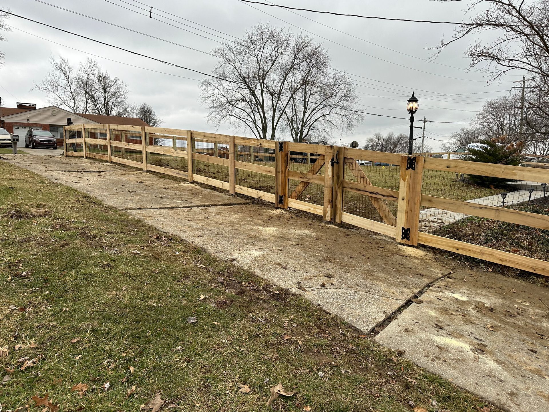 Wooden fence with gate along a gravel driveway; overcast sky.