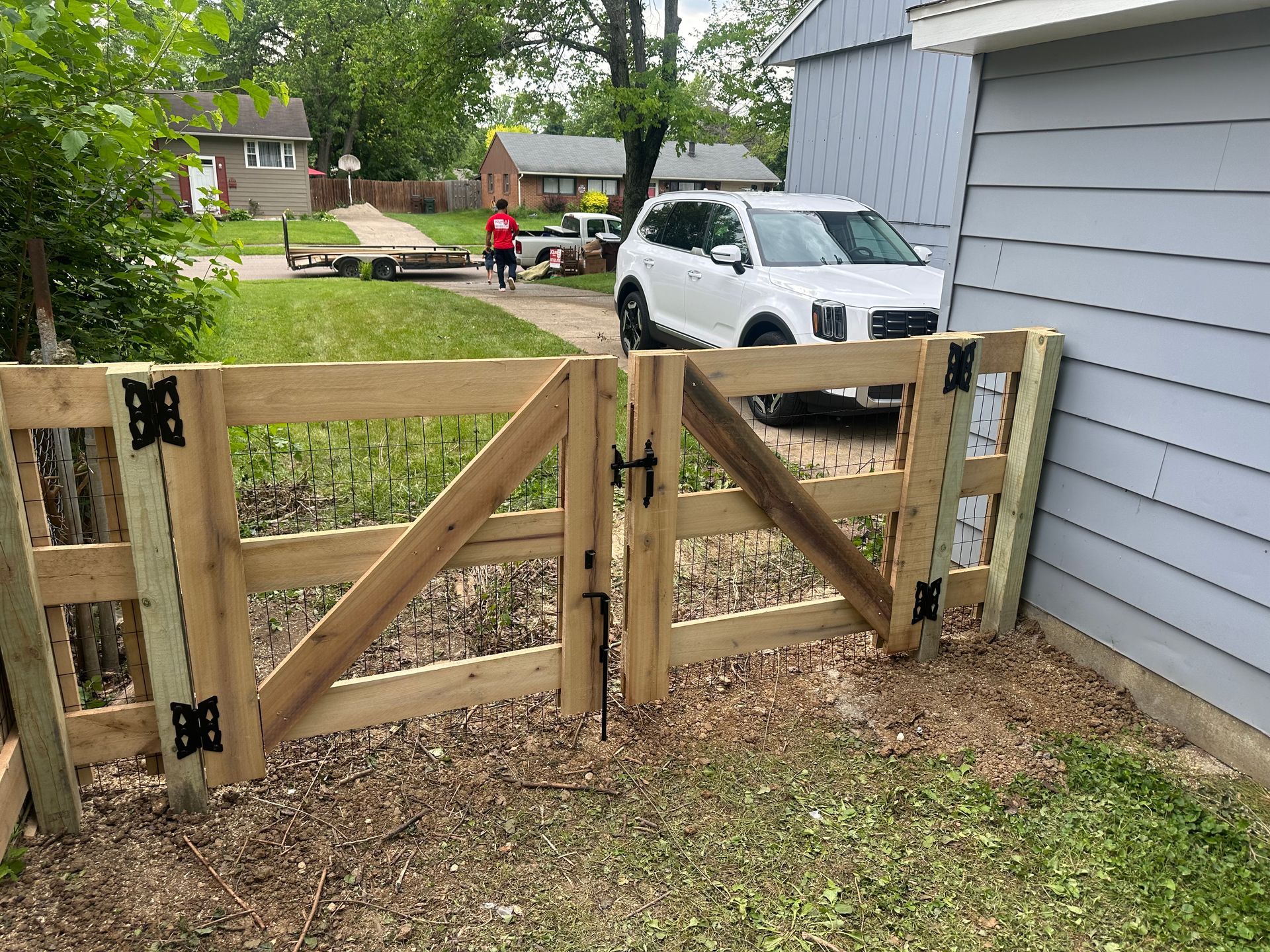 Wooden gate with black hardware, next to a blue house, and a white SUV in the background.
