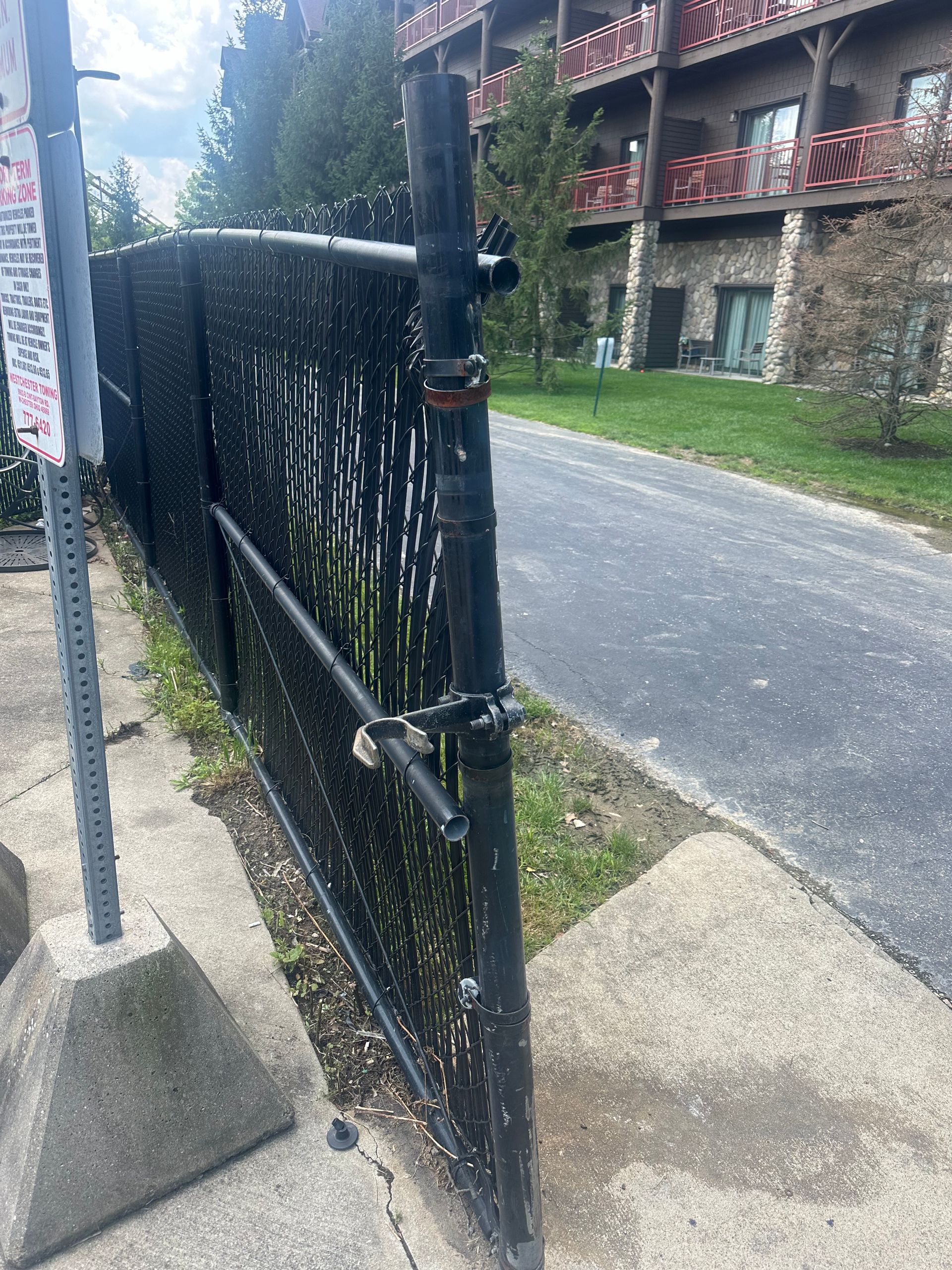 Black fence with opaque screening along a walkway, building in the background.