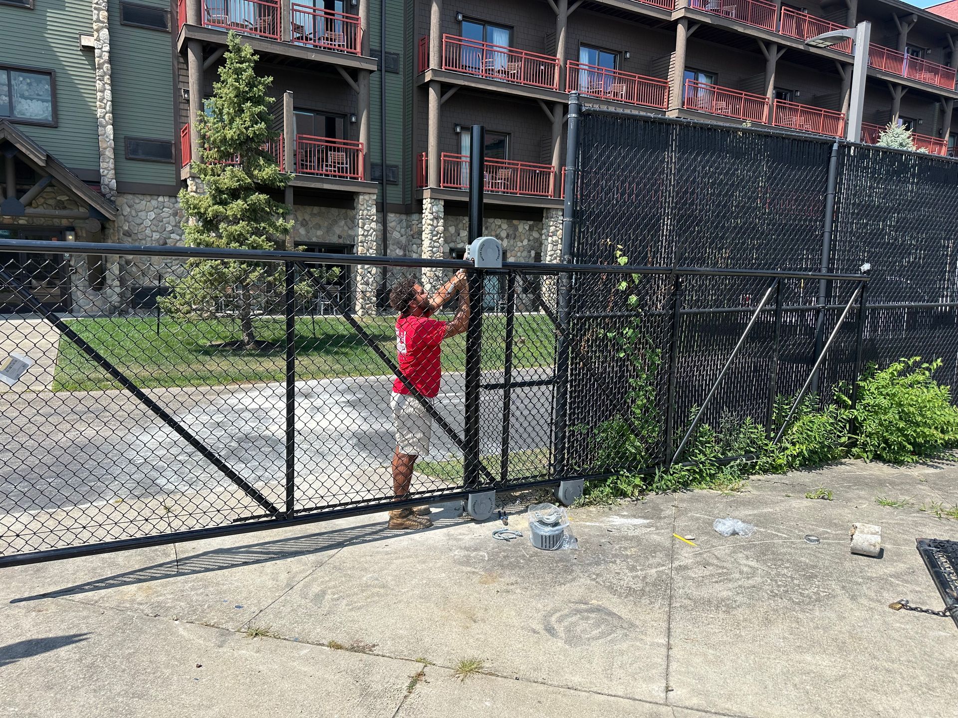 Person in red shirt opening a black metal gate with a hotel in the background.