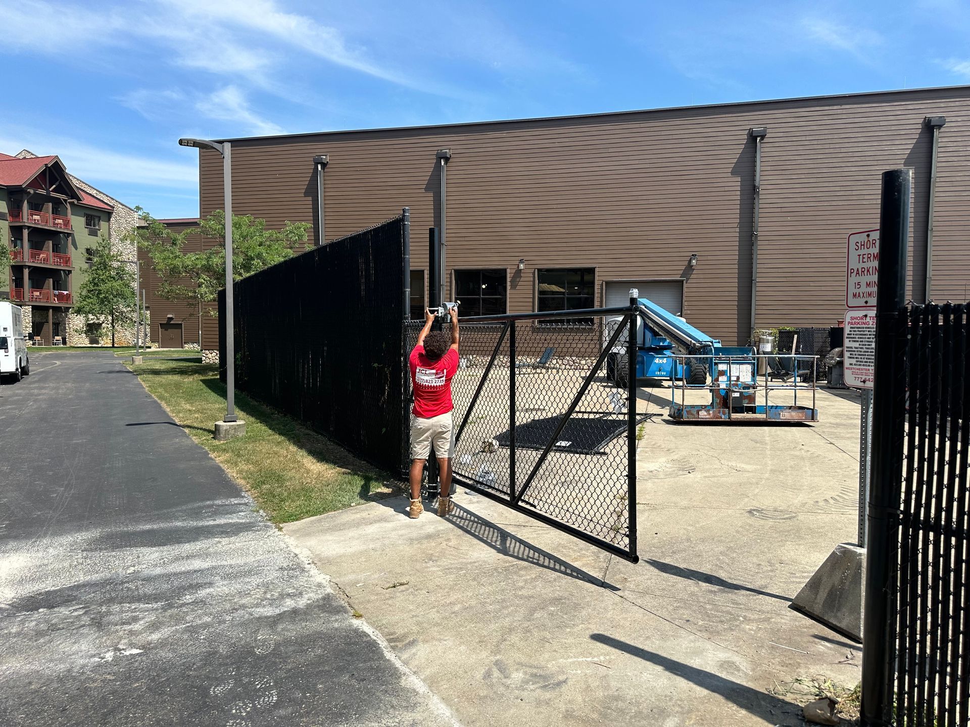 Person opening a black metal gate next to a black fence, leading to a building.