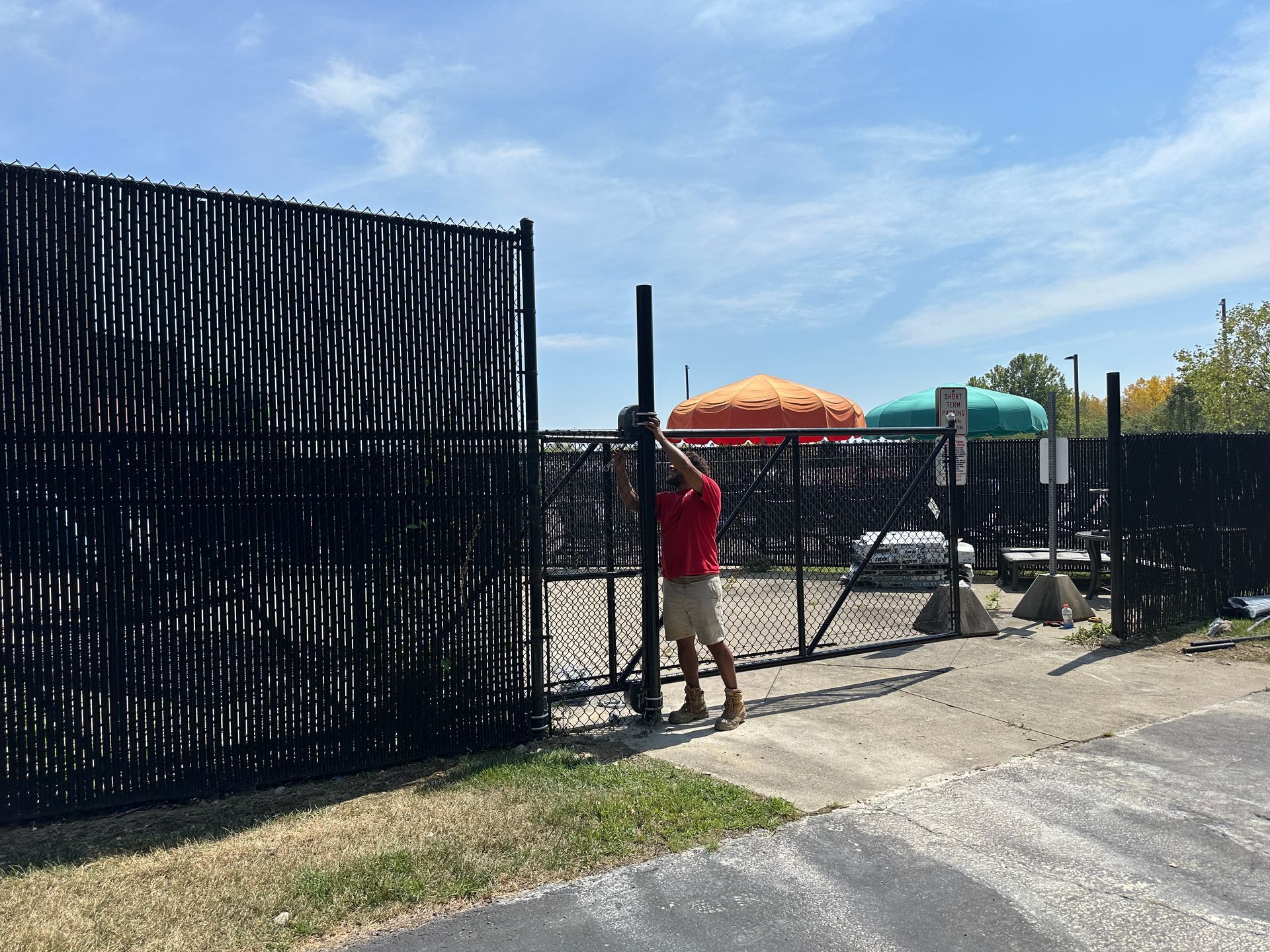 Person in red shirt installing a black metal fence post next to an existing black fence.