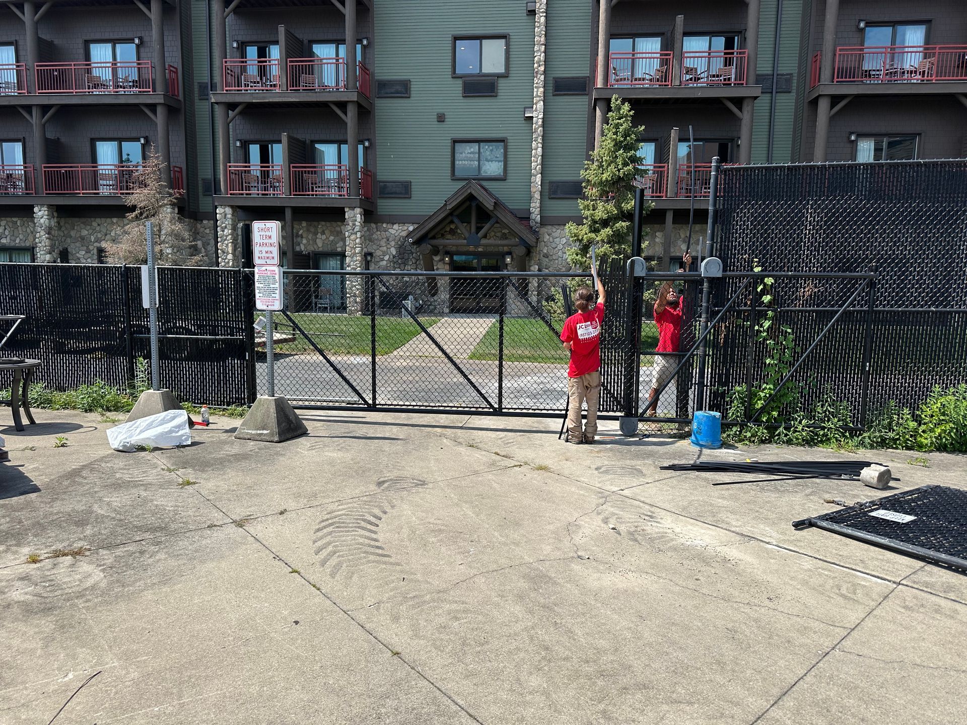 Two people in red shirts by a gate, near a building.