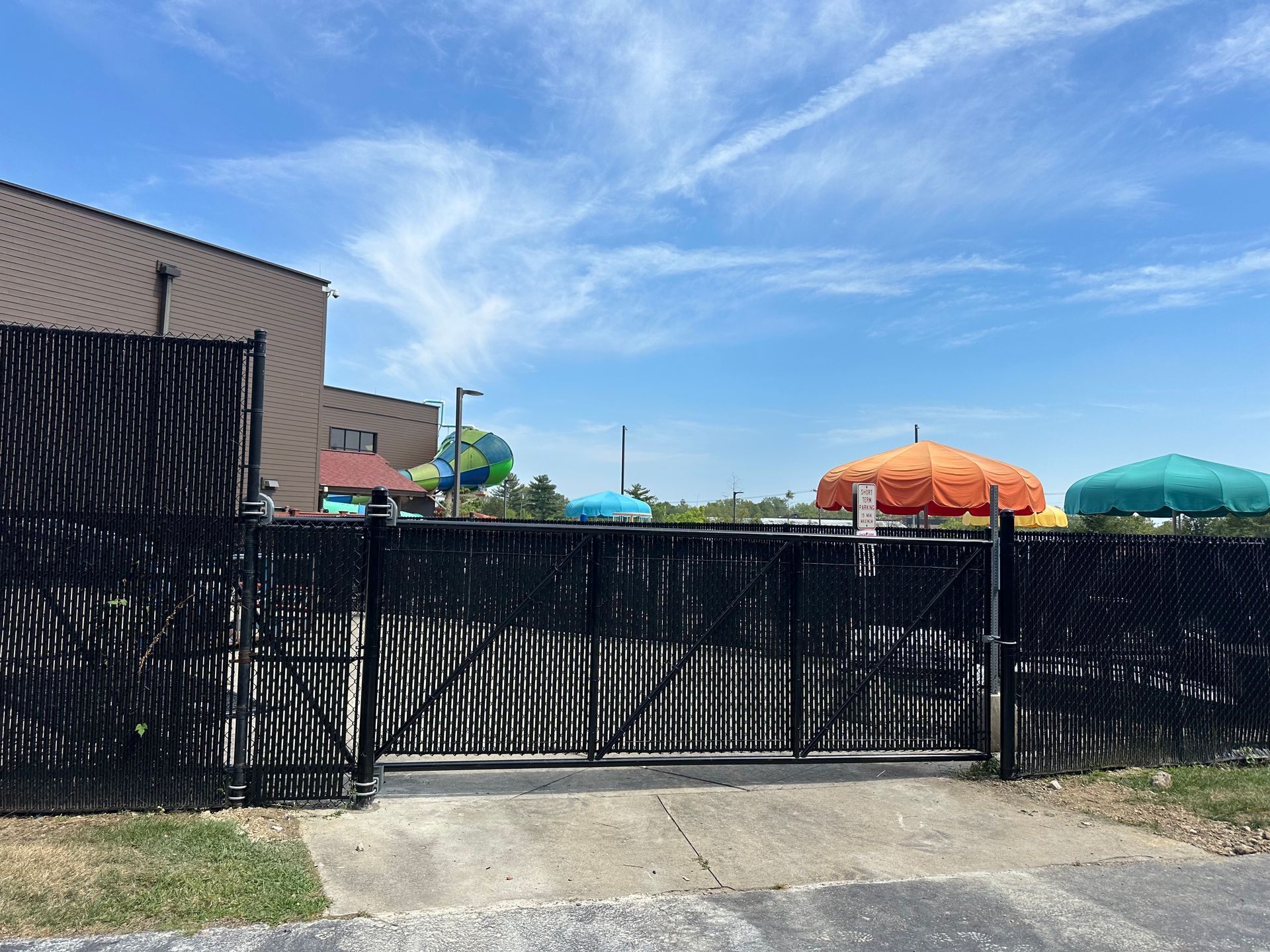 Black gate and fence in front of a colorful umbrella-filled area, under a blue sky.