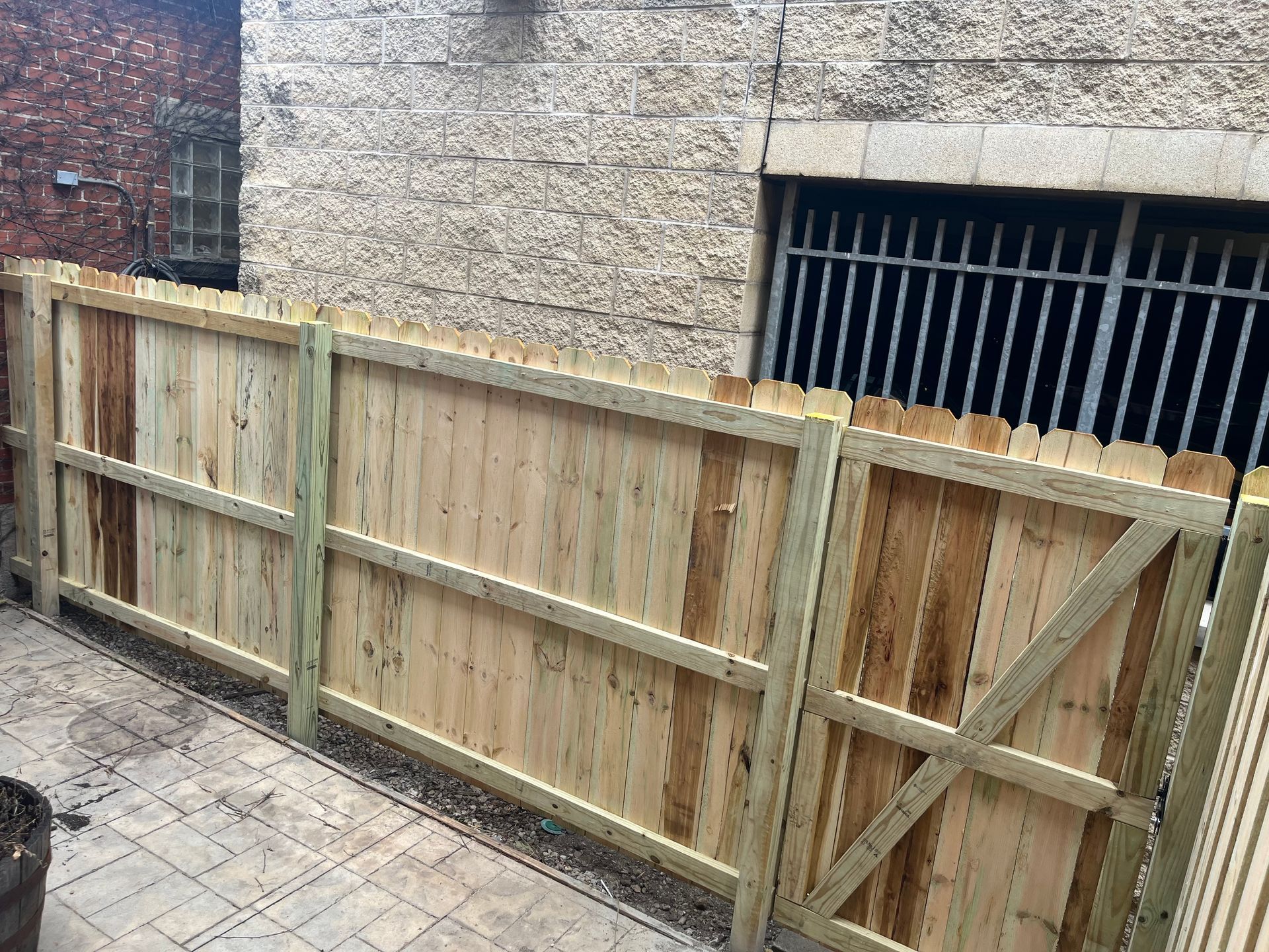 Wooden fence in an alleyway, beside a concrete wall with barred window.