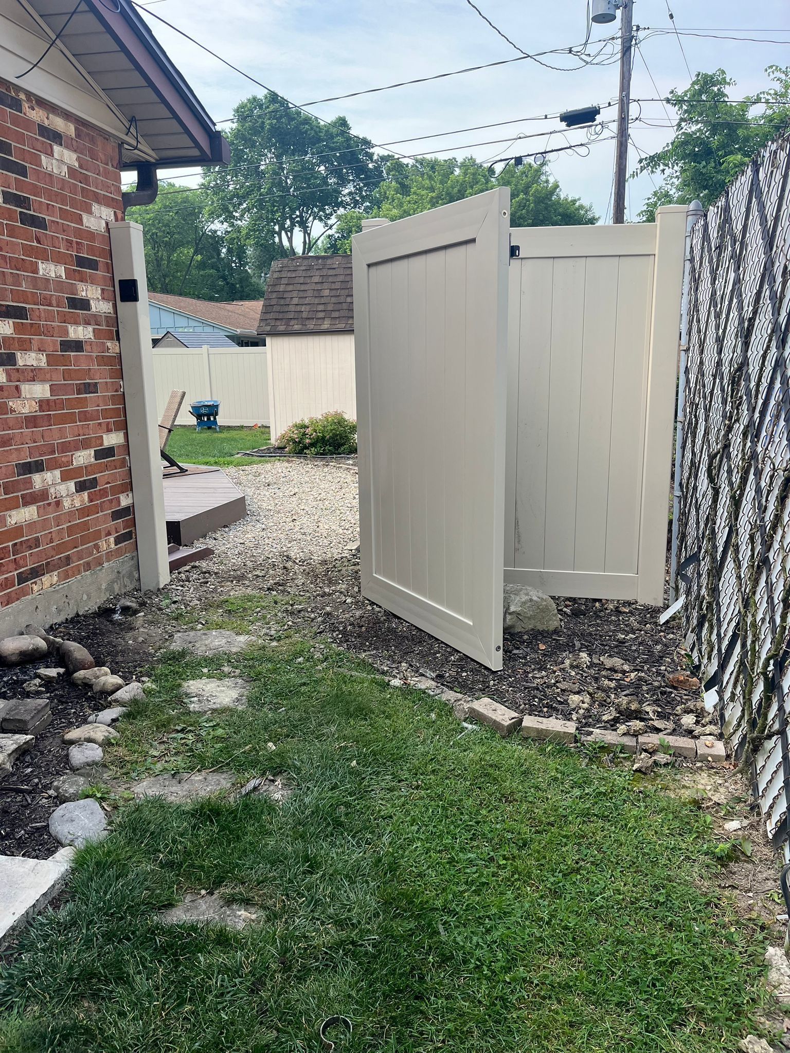 Beige vinyl fence gate in residential backyard. Green grass and brick building visible.