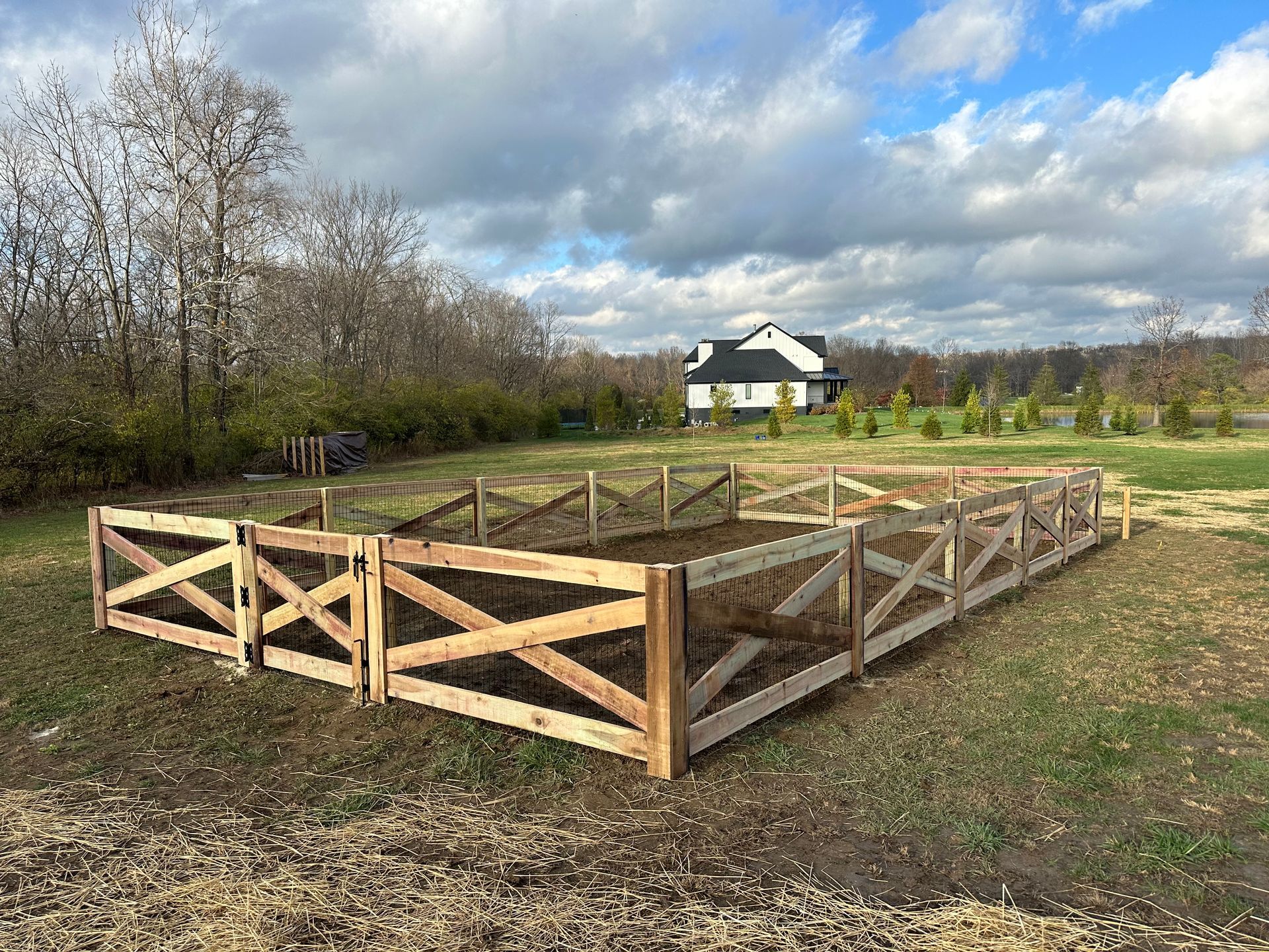 Wooden fenced garden in grassy yard, house and trees in background under cloudy sky.