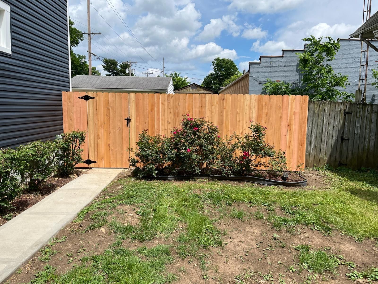 Wooden fence with gate in a yard; bushes and walkway in front.