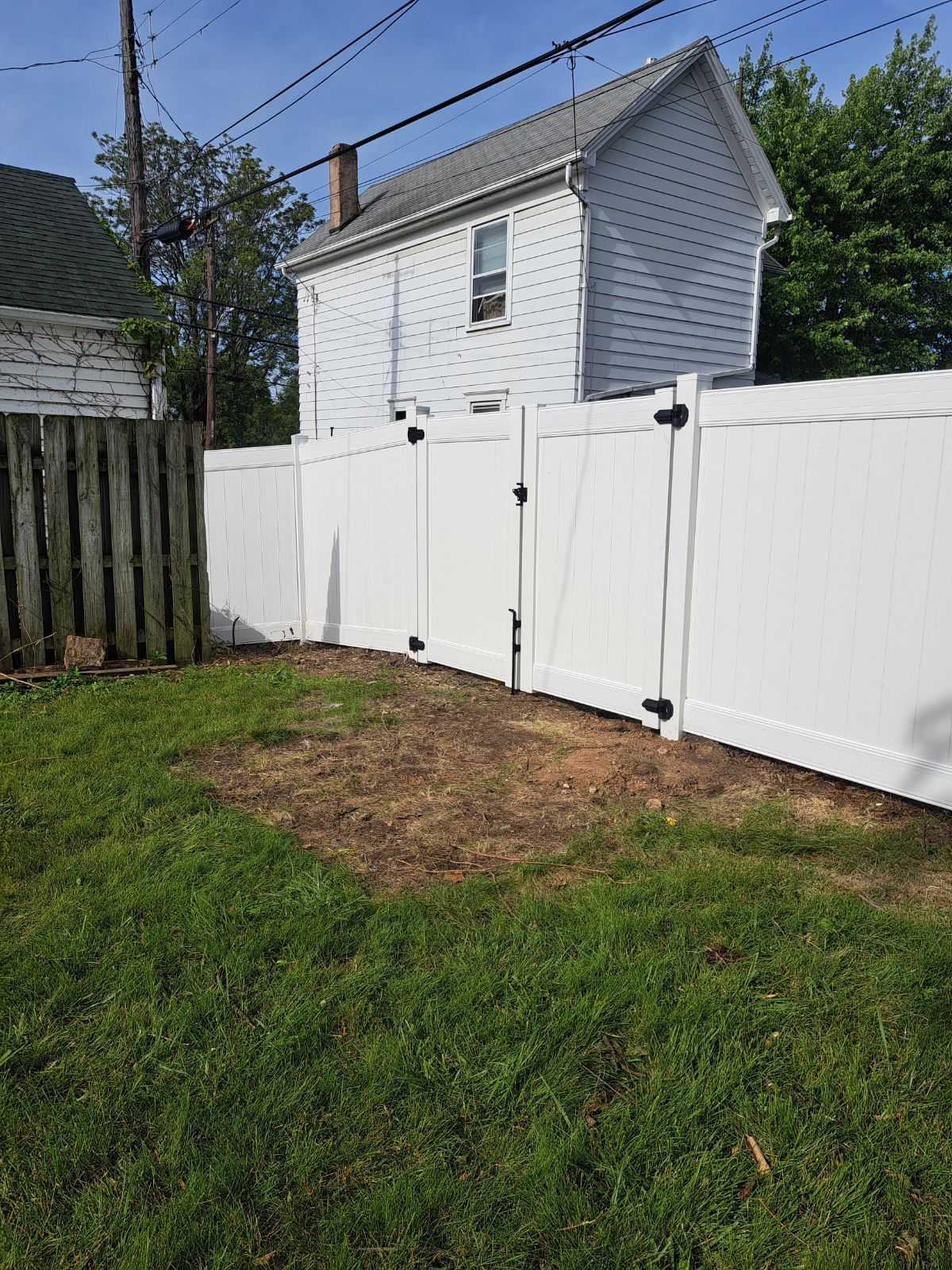 White vinyl fence enclosing a grassy backyard, adjacent to a weathered wooden fence and a light-colored house.