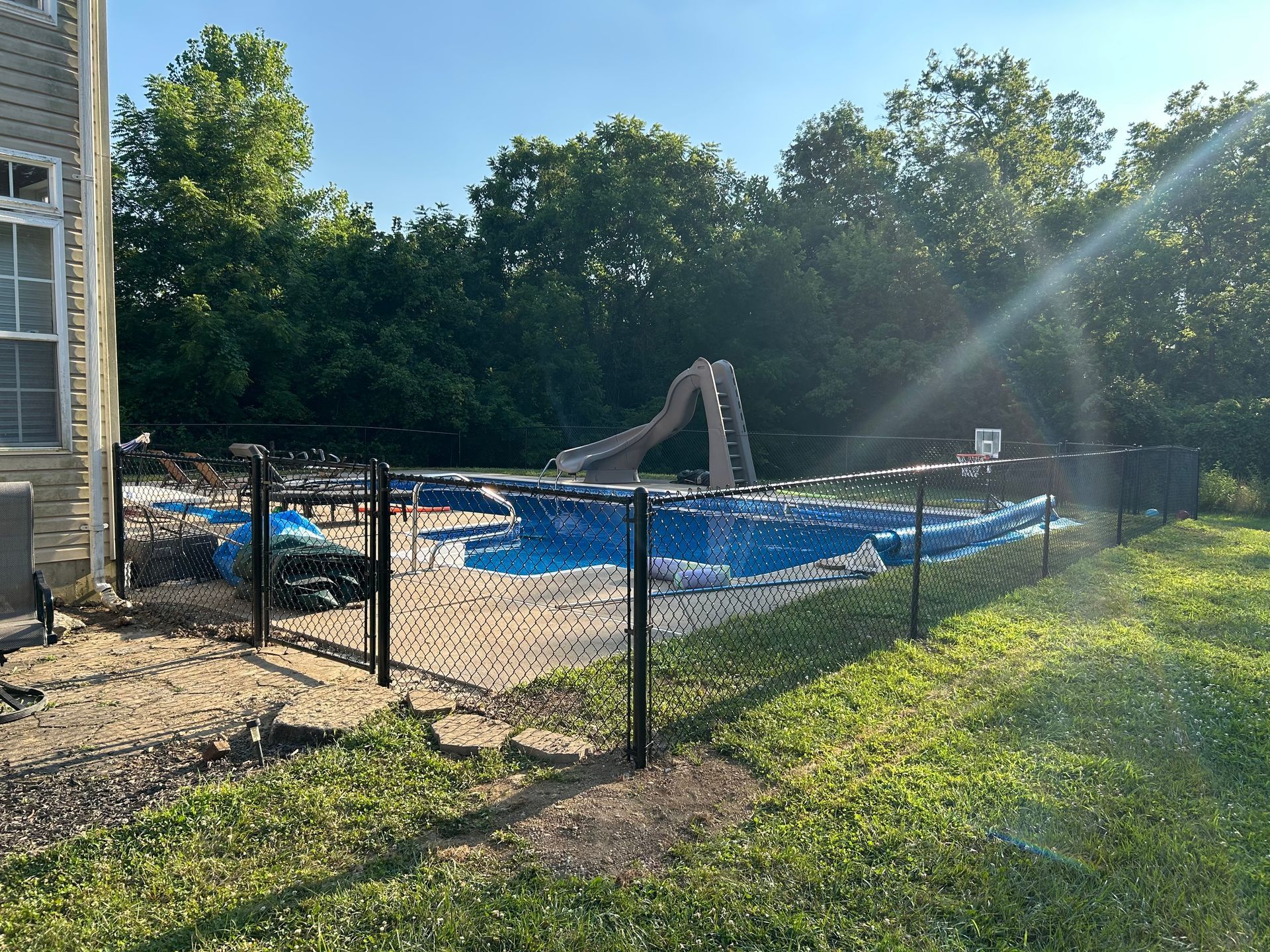 Above-ground pool with slide, enclosed by black fence, on a sunny day in a backyard.