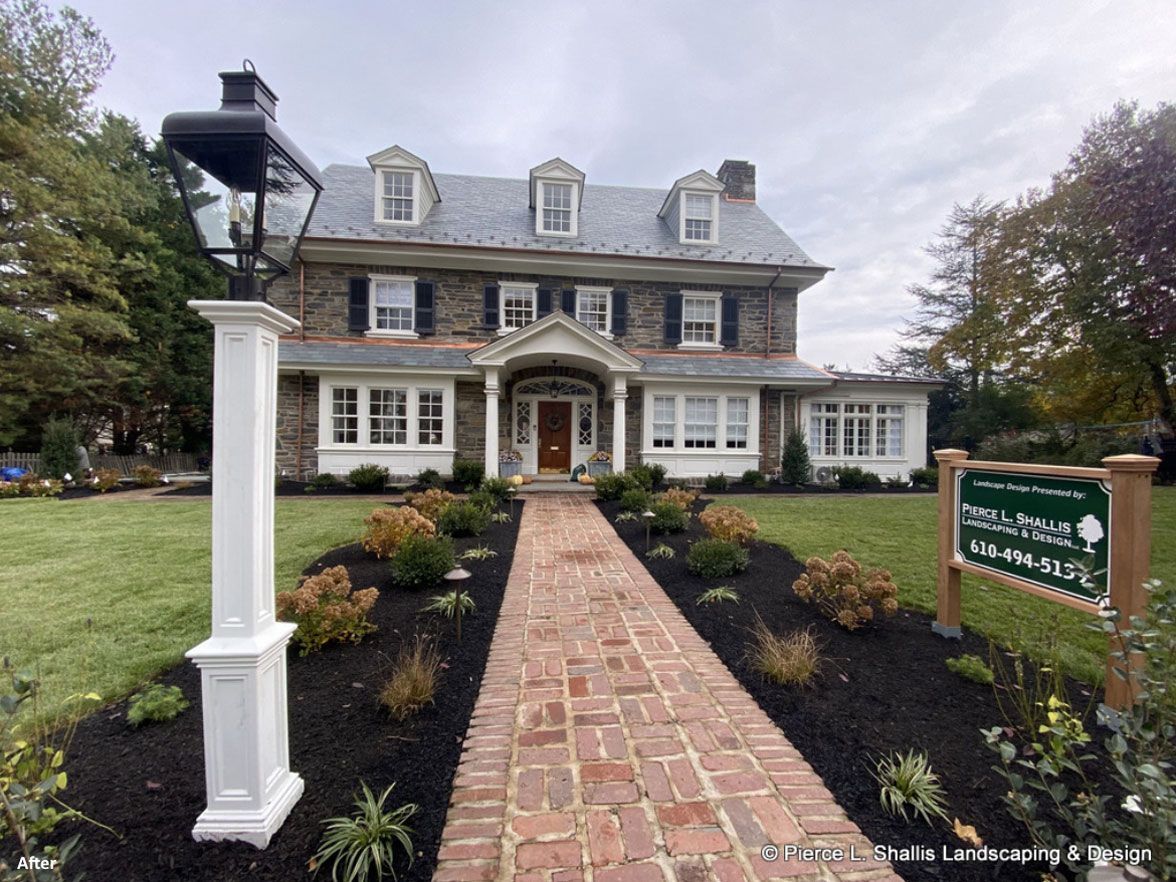 Historic stone building with white trim, centered brick walkway, and landscaped front entrance under overcast sky