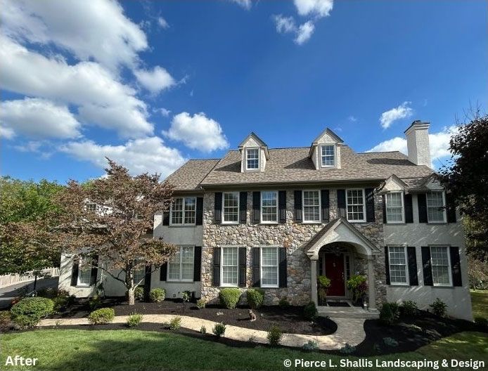Gray two-story house with white shutters, manicured landscaping, and blue sky