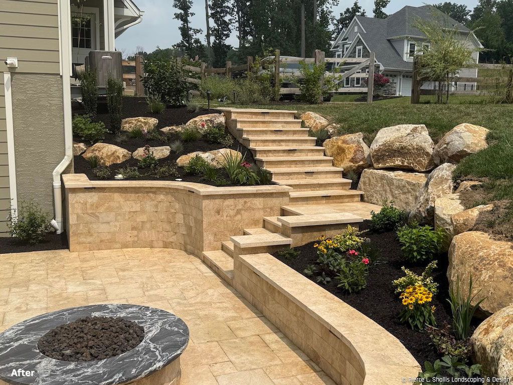 Stone patio with curved retaining wall, steps, landscaped rocks, and a fire pit in a backyard.