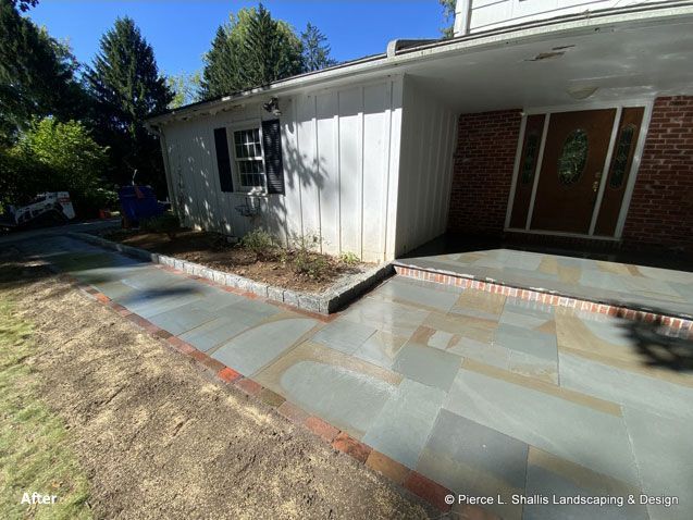 Modern house entry patio with light gray stone pavers, brick walls, and landscaped planter beds