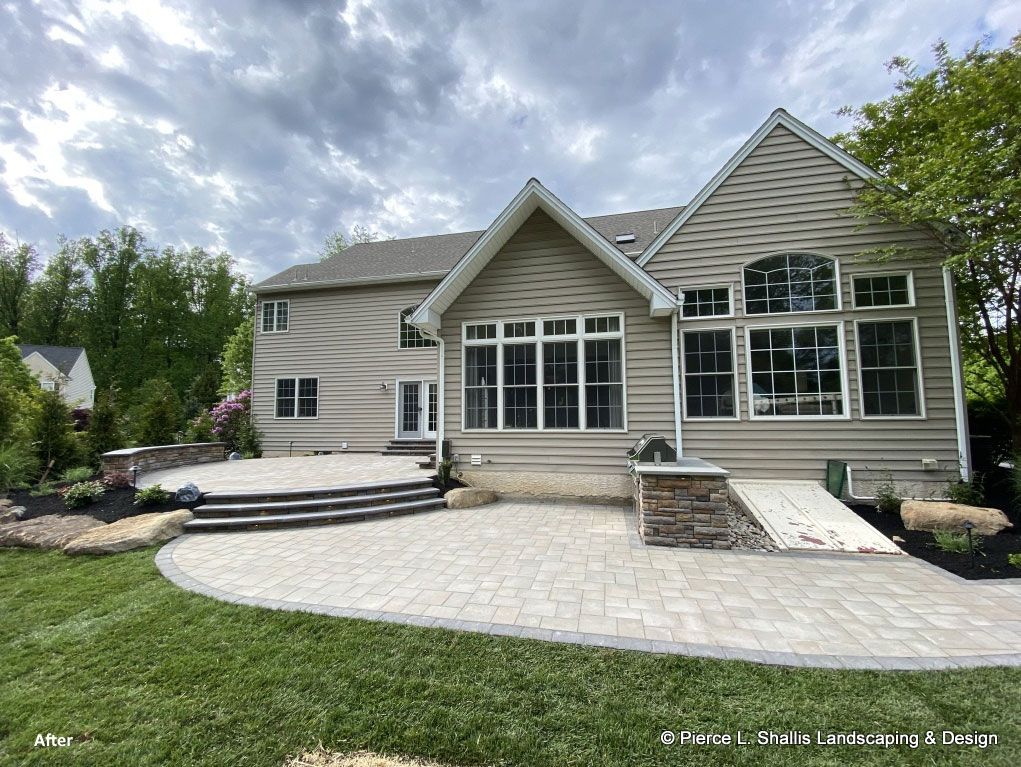 Modern house exterior with stone patio, large windows, and landscaped yard