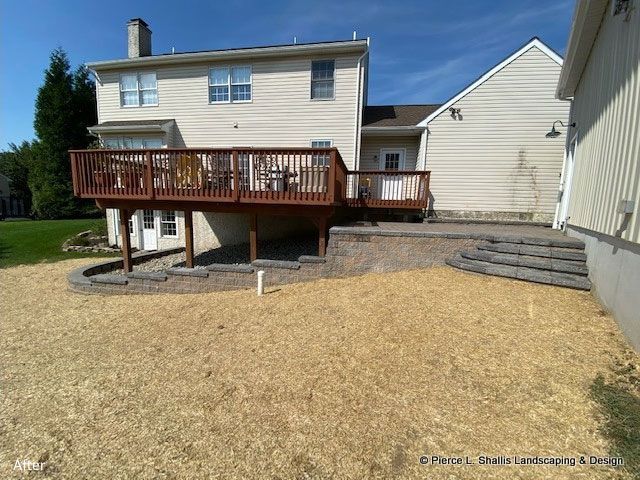 Backyard with raised wooden deck, gravel patio, and beige house under a blue sky