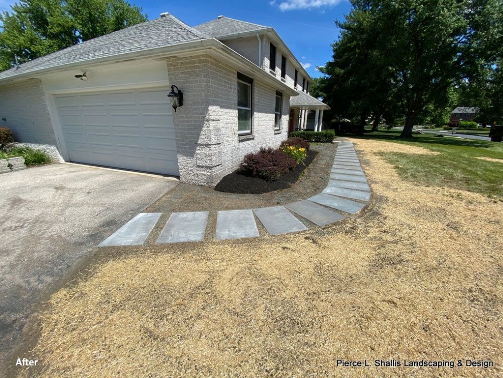 Suburban house with white garage, stone walkway, and dry lawn under a blue sky