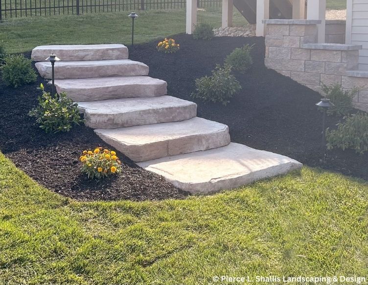 Stone front steps with dark mulch, yellow flowers, and a green lawn in a landscaped yard