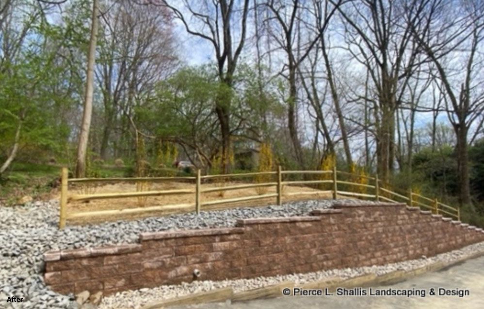 Wooden fence and stone retaining wall on a sloped wooded landscape with bare trees