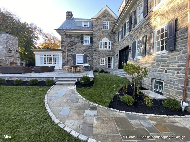 Stone house courtyard with curved walkway, manicured lawn, and large windows