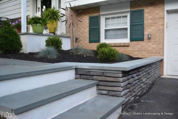 Front steps and a stacked-stone retaining wall by a brick house with green shutters and potted plants