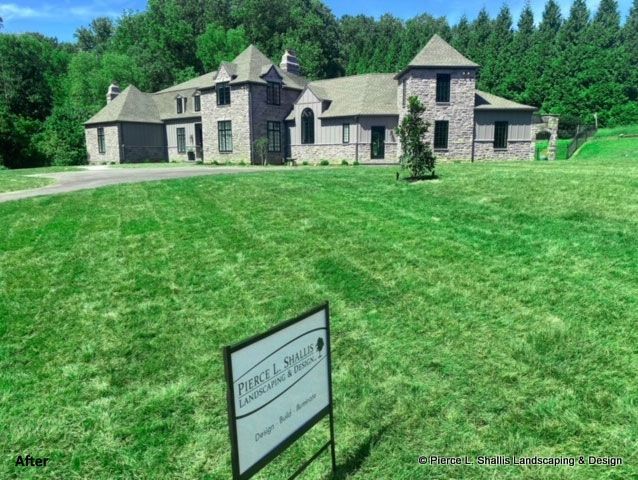 Large stone house with green lawn and a real estate sign in front