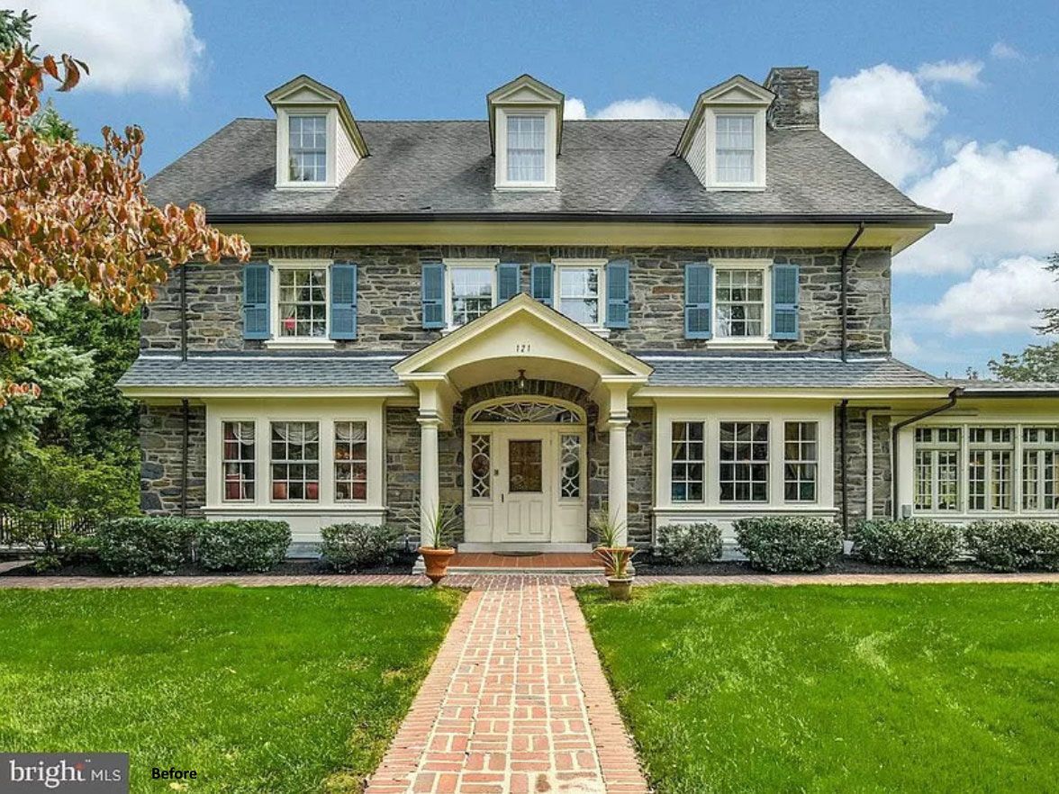 Large gray two-story house with white trim, dormer windows, and a front brick walkway leading to the entrance
