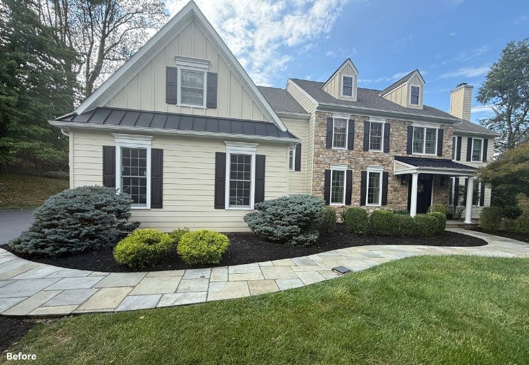 Suburban house with beige siding and stone facade, curved stone walkway, and manicured lawn under a blue sky