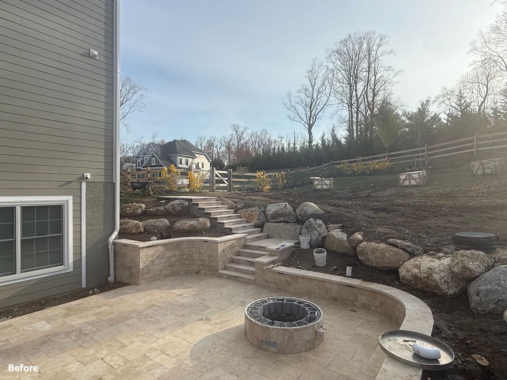 Backyard patio with stone steps, retaining wall, fire pit, and grill beneath a leafless hillside.