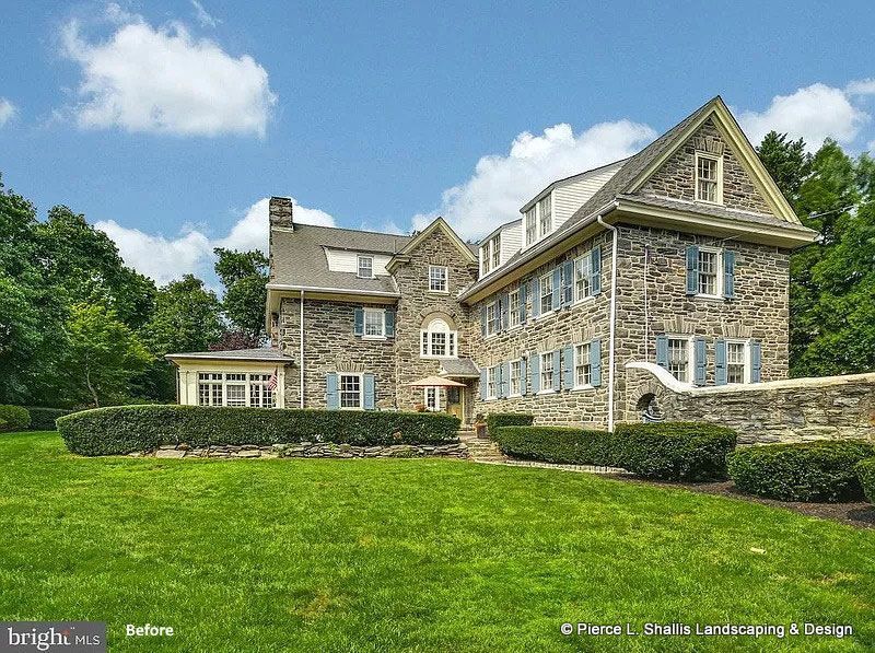 Stone mansion with manicured lawn, hedges, and blue sky.