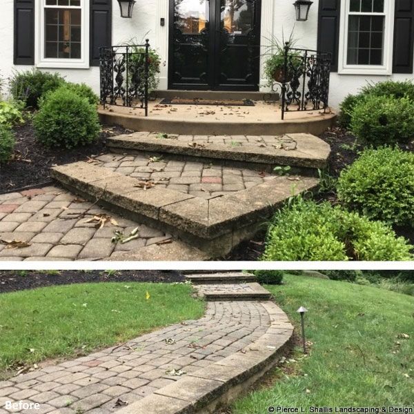 Cracked stone front steps and walkway leading to a black double door, with shrubs and a curved path.
