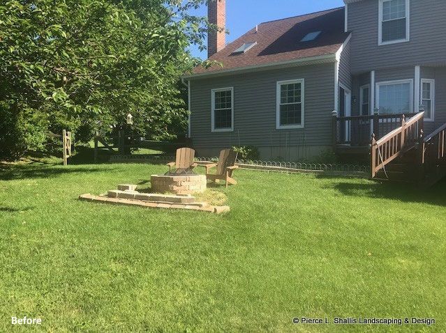 Backyard with a small stone patio and a gray house with a deck and stairs
