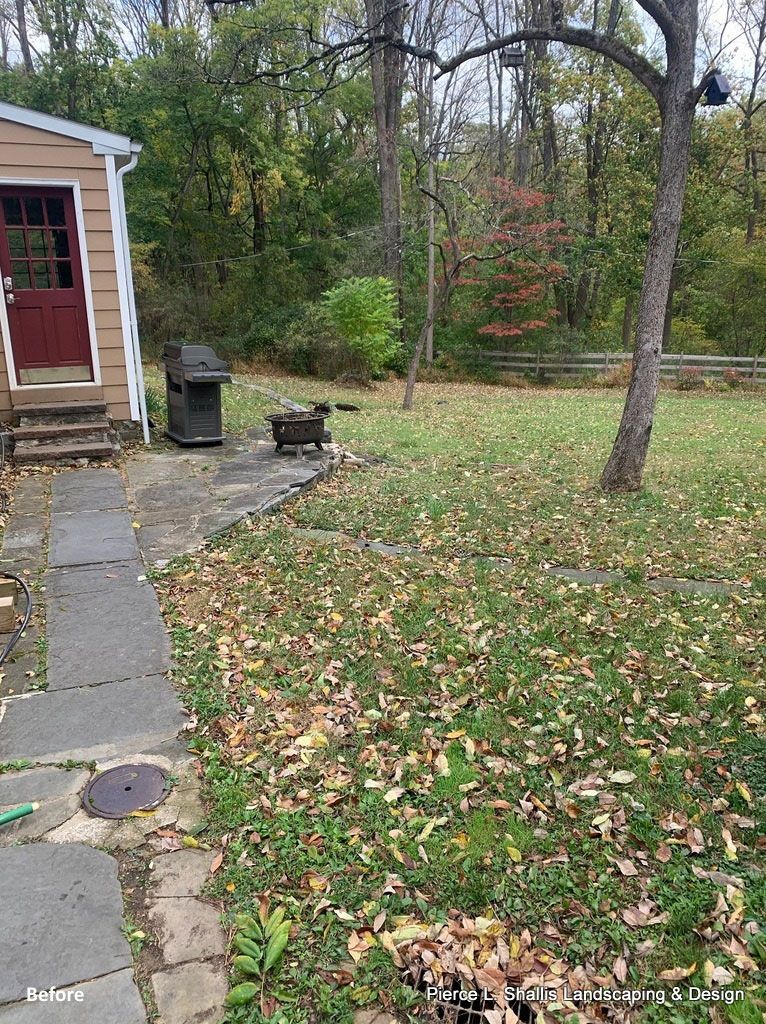 Stone walkway beside a beige house leading to a red door, with a lawn and trees in fall.