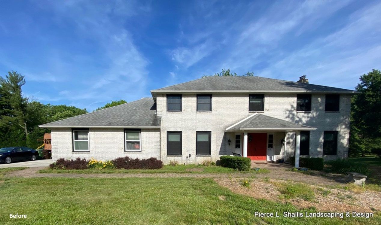 Two-story white house with a red front door, gray roof, and green lawn under a blue sky.