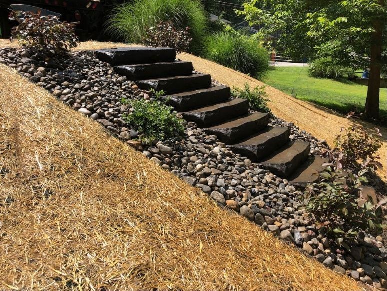 Stone steps in a landscaped garden beside a rocky slope and mulch-covered hillside.